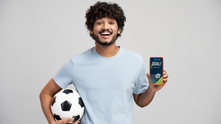 homem segurando uma bola de futebol e um celular com um aplicativo de apostas aberto